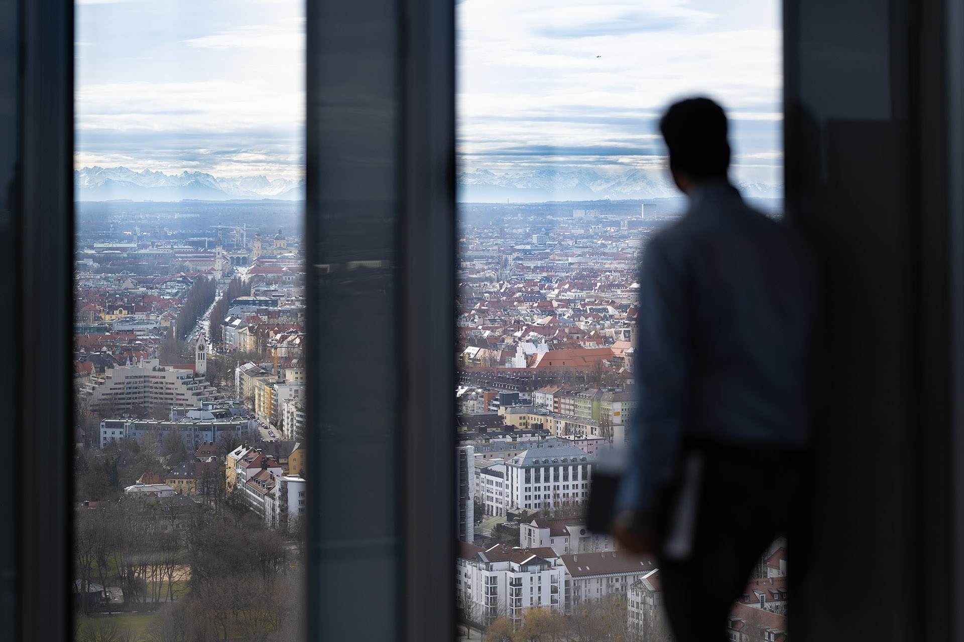 Cloudfalke consultant looking out over the city skyline from a high-rise office with mountains in the background